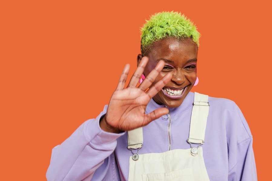 a black woman with green hair smiling shyly