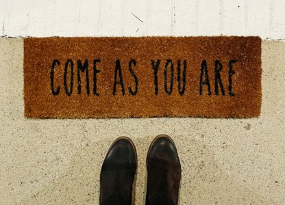 feet at a door mat that says come as you are