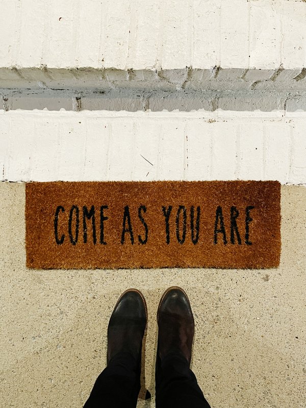 feet at a door mat that says come as you are